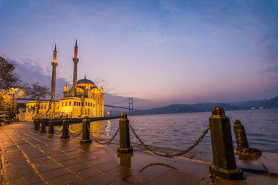 Mosque by river in city against sky during sunset