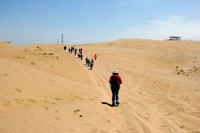 People with flag walking on desert against sky