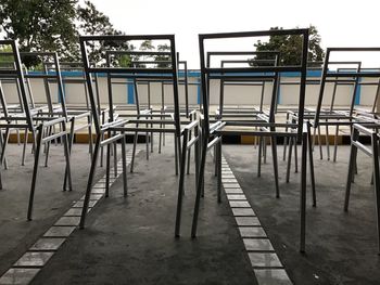 Empty chairs and tables by swimming pool against clear sky