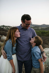 Father standing with son and daughter on field during sunset