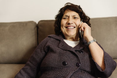 Portrait of smiling young woman using phone while sitting on sofa