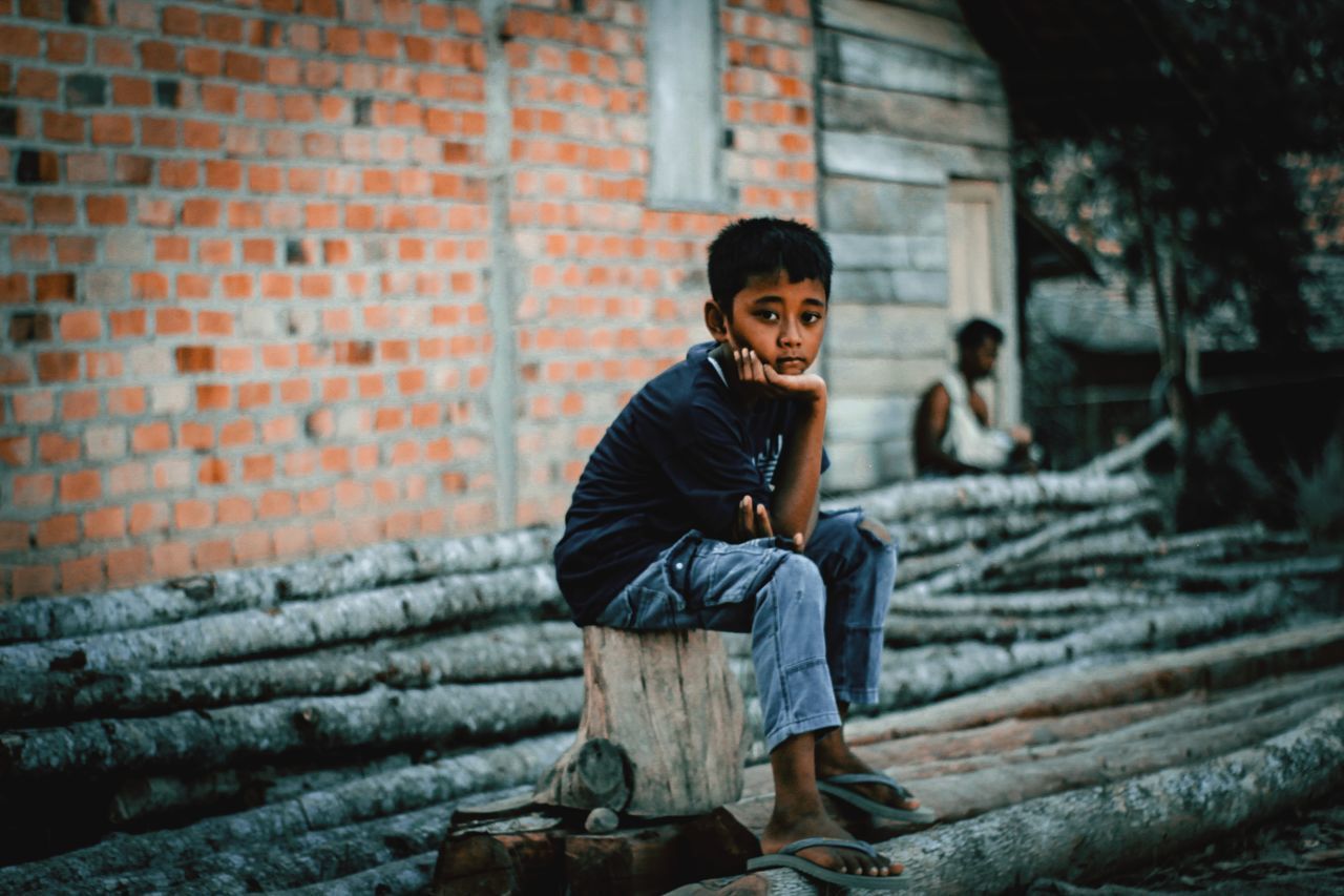 PORTRAIT OF A SMILING BOY AGAINST BRICK WALL