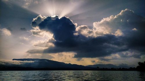 Sunlight streaming through clouds over lake against sky