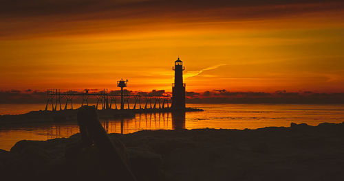 Silhouette lighthouse by sea against orange sky