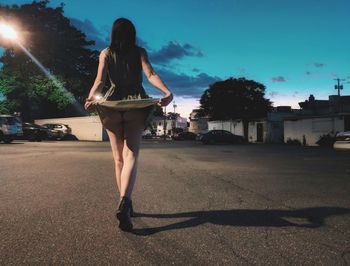 Rear view of woman holding dress while walking on road at night