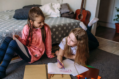 Two girls friends play at home, draw with pencils and felt-tip pens and have fun