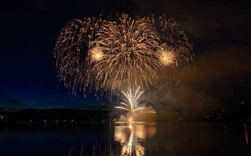 Firework display over lake against sky at night