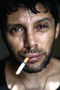 Close-up portrait of man with cigarette against black background