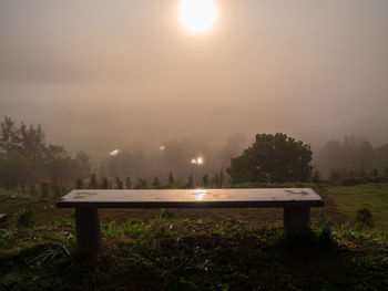 Empty bench on field against sky during foggy weather