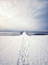 Footprints on snow covered landscape against sky