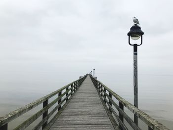 Street lights on pier by sea against sky