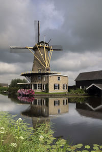 Traditional windmill by lake against sky