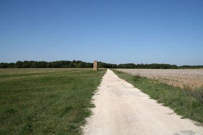Road leading towards field against clear sky