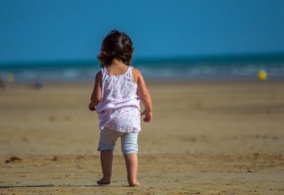 Rear view of girl at sandy beach against clear sky