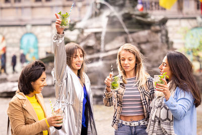 Friends enjoying drinks by a fountain, cherishing happy moments and socializing outdoors