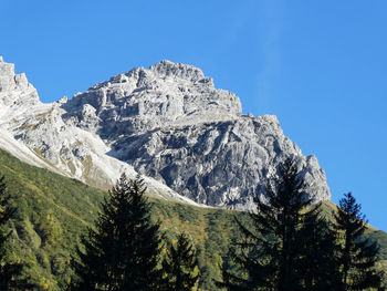 Low angle view of snowcapped mountains against clear blue sky