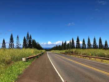 Empty road along plants and trees against blue sky