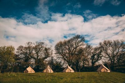 Tents on field by trees against cloudy sky