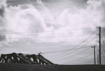 Silhouette of bridge and power lines against cloudy sky