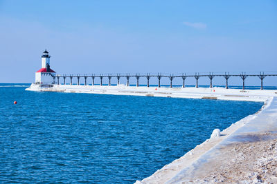 Lighthouse by sea against clear blue sky