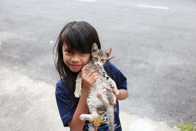 Portrait of girl holding cat while standing on road