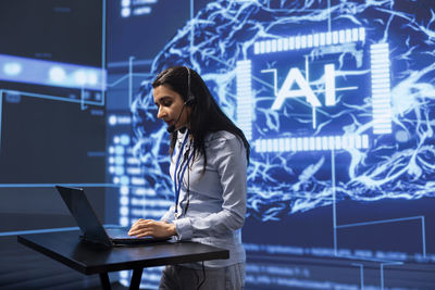 Portrait of young woman using laptop while standing in city at night