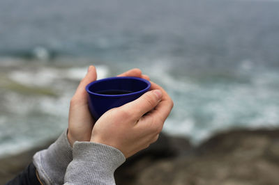 Midsection of woman holding coffee cup at sea shore