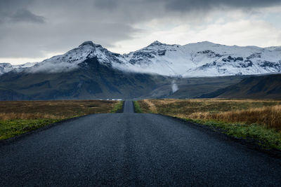 Road towards the scenic snow covered mountains  in the rural countryside of south iceland