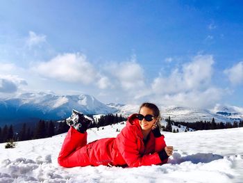Woman wearing sunglasses lying on snow covered land against sky