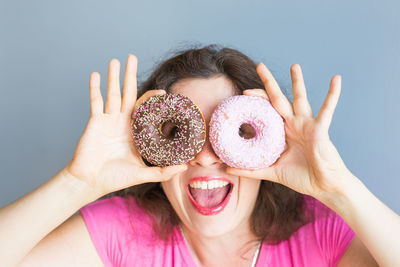 Cheerful woman holding donuts against wall