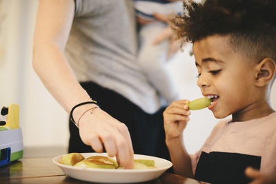 Boy having food while sitting by mother at home