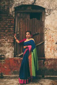 Young woman standing against old abandoned house