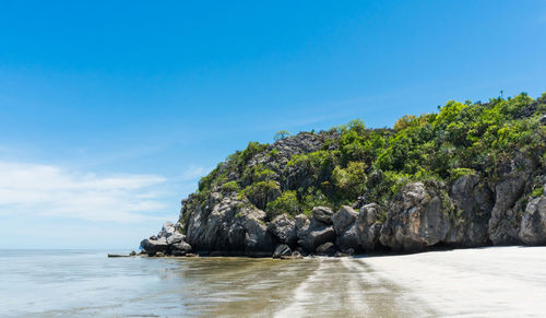 Scenic view of rocks by sea against blue sky