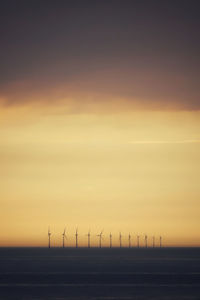 Wind turbines at sea against sky during sunset