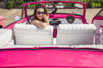 Portrait of smiling woman sitting in pink car