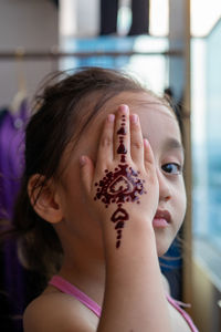 Portrait of henna ornaments on little girl's hand covering face.