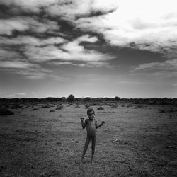 Portrait of shirtless boy standing on dirt road against sky