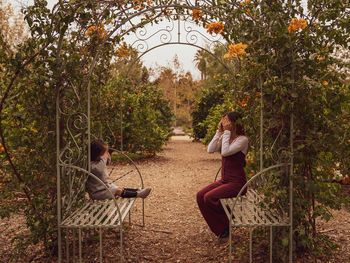 Woman sitting by plants against trees