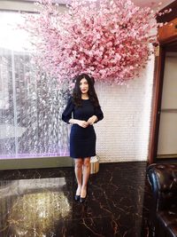 Full length portrait of woman standing against pink flowers