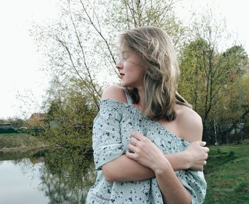 Beautiful young woman with arms raised against trees