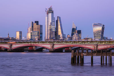 Bridge over river by buildings against sky in city