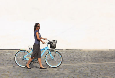 Woman with bicycle walking on footpath against wall