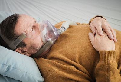 High angle view of man wearing oxygen mask while lying on bed in hospital