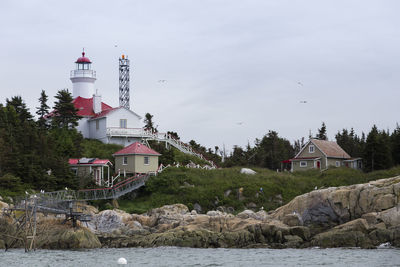 Lighthouse by river and buildings against sky