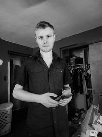 Portrait of young man standing with mobile phone at home