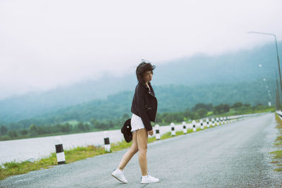 Side view of woman standing on road against mountain