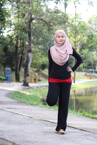 Portrait of mid adult woman wearing hijab while exercising by lake at park