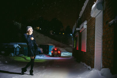 Full length of young woman smoking cigarette during snowfall at night