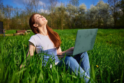 Young woman using laptop while sitting on grassy field