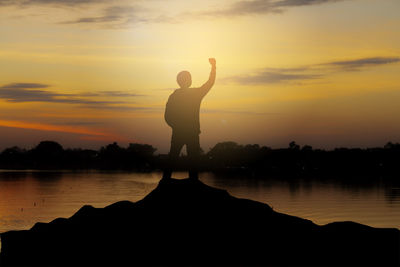 Silhouette man standing by lake against sky during sunset